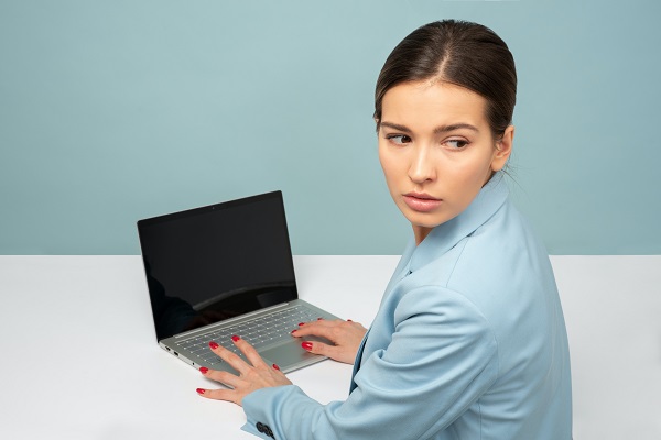 Une jeune femme regarde par dessus son épaule si quelqu'un observe son pc.